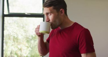 Düşünceli beyaz bir adam pencereden dışarı bakıyor ve kahve içiyor. ev hayatı ve evde boş zaman.