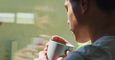 Afro-Amerikalı bir adam pencereye bakıyor ve evde kahve içiyor. Boş zaman, evde tek başına dinlenmek..