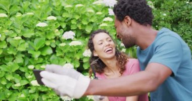 Melez çiftler bahçesinde çiçeklerle selfie çekiyorlar. Bahçıvanlık, bahçıvanlık ve bahçe işleri..