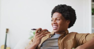 Mutlu Afro-Amerikan adam evde akıllı telefon kullanıyor. Teknoloji kullanarak boş zaman geçirmek, evde tek başına dinlenmek..
