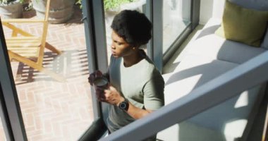 Afro-Amerikalı bir adam pencereye bakıyor ve evde kahve içiyor. Boş zaman, evde tek başına dinlenmek..