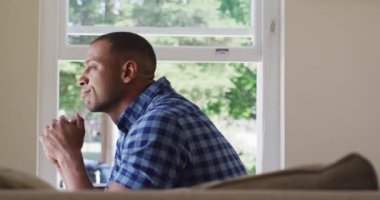 Düşünceli, melez bir adamın pencereden dışarı bakması. boş zamanlarını evde geçirirler..