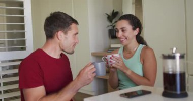 Kafkasyalı mutlu bir çift kahve içiyor ve akıllı telefon kullanıyor. Teknoloji kullanarak evde vakit geçirmenin tadını çıkarıyorum..