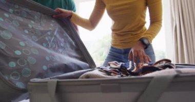 Çift ırklı çiftin seyahat için bavullarını topladıktan sonra sevinçle el çırpışları. Tatil seyahatine hazırlanıyorum..