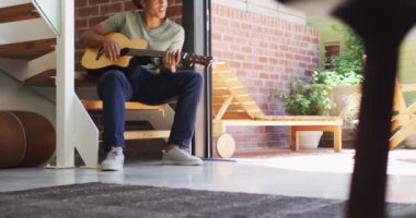 Mutlu Afrikalı Amerikalı adam gitar çalıyor ve evde şarkı söylüyor. Boş zaman, evde tek başına dinlenmek..