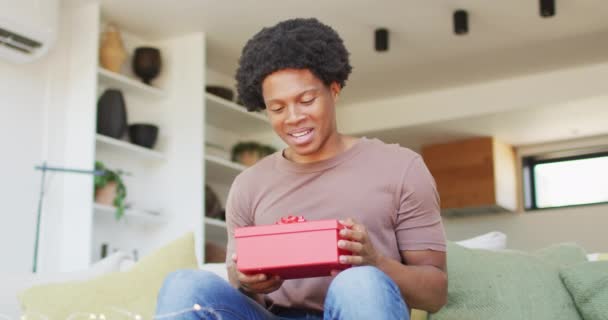 アフリカ系アメリカ人の男性が家で贈り物を開く 余暇はテクノロジーを使って一人で家でリラックスし — ストック動画