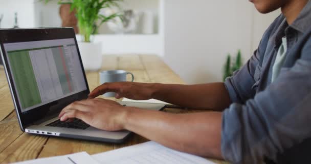 アフリカ系アメリカ人の男性が自宅でノートパソコンを使って働いています 技術を使って遠隔地から働き — ストック動画