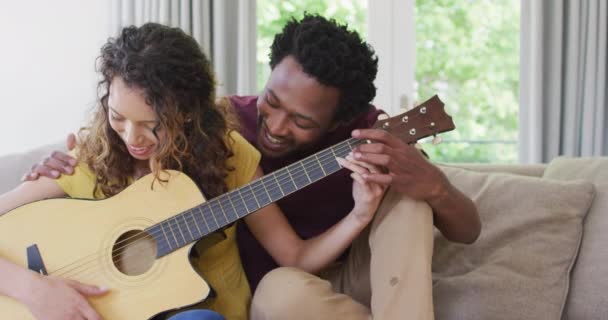 幸せな出産のカップルが一緒にソファに座ってギターを演奏します 家庭で質の高い余暇を過ごすことができます — ストック動画