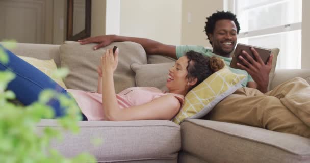 Happy Biracial Couple Relaxing Sofa Smartphone Tablet Enjoying Quality Leisure — Stock Video