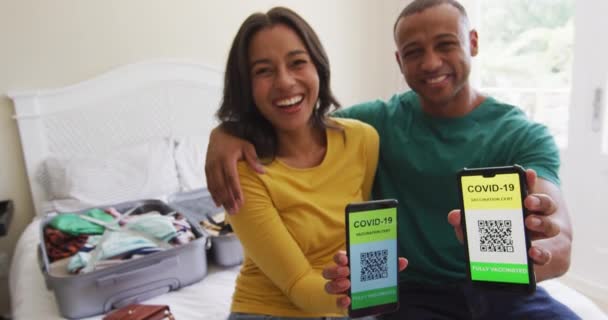 Gelukkig Biracial Paar Zitten Bed Toont Smartphones Met Covid Paspoorten — Stockvideo