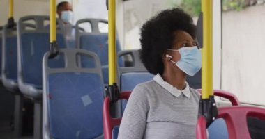Otobüste oturan yüzü maskeli Afrikalı Amerikalı iş kadını. Dijital göçebe covid 19 salgını sırasında şehirde dolanıyor..
