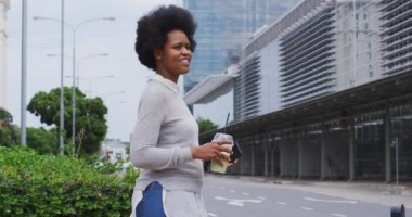 Afrika kökenli Amerikalı iş kadını şehirde akıllı telefon ve kahveyle yürüyor. Dijital göçebe şehirde geziyor, dolaşıyor..