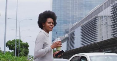 Afrika kökenli Amerikalı iş kadını şehirde akıllı telefon ve kahveyle yürüyor. Dijital göçebe şehirde geziyor, dolaşıyor..