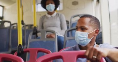 Otobüste oturan yüzü maskeli Afro-Amerikan erkek ve kadın. Dijital göçebe covid 19 salgını sırasında şehirde dolanıyor..
