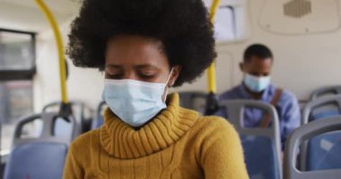 Otobüste oturan yüzü maskeli Afrikalı Amerikalı iş kadını. Dijital göçebe covid 19 salgını sırasında şehirde dolanıyor..
