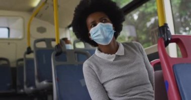 Otobüste oturan yüzü maskeli Afrikalı Amerikalı iş kadını. Dijital göçebe covid 19 salgını sırasında şehirde dolanıyor..
