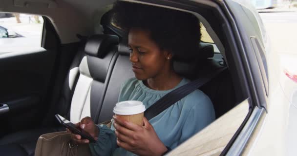 アフリカ系アメリカ人のビジネスマンがスマートフォンを使い 車の中でテイクアウトコーヒーを持っている 外にも街中にもデジタル ノマドが — ストック動画