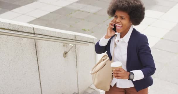 アフリカ系アメリカ人のビジネスマンがテイクアウトコーヒーを持っていて スマートフォンで話している 外にも街中にもデジタル ノマドが — ストック動画