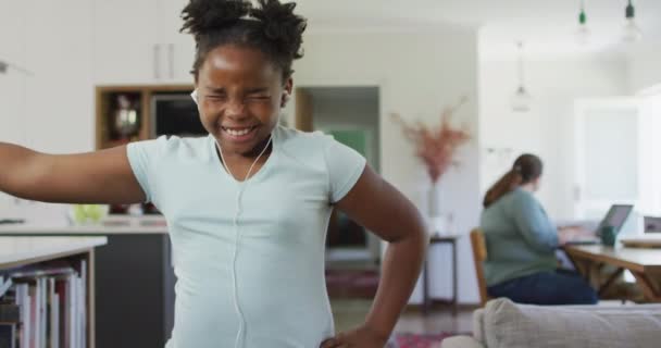 幸せなアフリカ系アメリカ人の少女は イヤホンを装着し リビングルームで踊ります 家庭生活や家での時間を — ストック動画