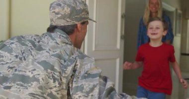 Caucasian male soldier embracing his smiling son over smiling wife and american flag. soldier returning home to family.