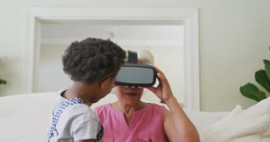 Mutlu Afro-Amerikan büyükanne oturma odasında torunu olan bir vr kulaklık kullanıyor. Aile evde birlikte vakit geçiriyor..