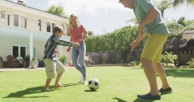 Happy caucasian couple with son playing football in garden. family spending time together at home.