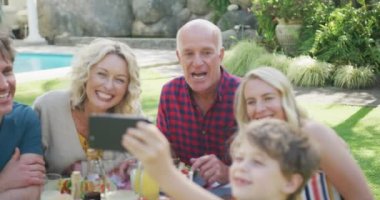 Kafkasyalı mutlu bir aile yemek yiyor ve bahçede selfie çekiyor. Aile evde birlikte vakit geçiriyor..