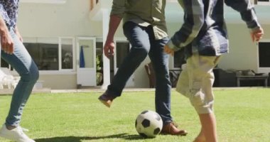 Happy senior caucasian couple with grandson playing football in garden. family spending time together at home.