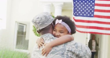 Amerikan bayrağı üzerinde gülümseyen kızını kucaklayan Afrikalı Amerikalı erkek asker. Asker evine, ailesine dönüyor..