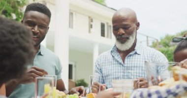 Mutlu Afro-Amerikan ailesi konuşuyor ve bahçede kahvaltı yapıyor. Aile birlikte dışarıda vakit geçiriyor..