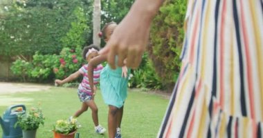 Afrikalı Amerikalı anne bahçede gülümseyen iki kızını kucaklıyor. Aile birlikte dışarıda vakit geçiriyor..