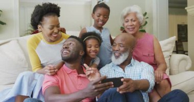 Mutlu Afro-Amerikan ailesi oturma odasında oturup akıllı telefon kullanıyor. Aile evde birlikte vakit geçiriyor..