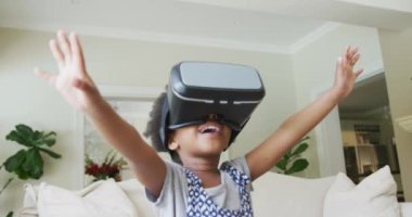 Gülümseyen Afrikalı Amerikalı kız oturma odasında VR kulaklıkla oynuyor. Evde yalnız zaman geçirmek..