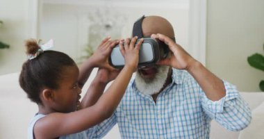 Mutlu Afro-Amerikan büyükbabası oturma odasında torunu ile vr kulaklık kullanıyor. Aile evde birlikte vakit geçiriyor..