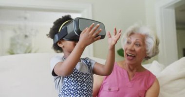 Mutlu Afro-Amerikan büyükannesi ve torunu oturma odasında vr kulaklık kullanıyor. Aile evde birlikte vakit geçiriyor..