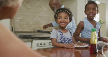 Torunları olan, kahvaltı yapan ve konuşan Afro-Amerikan büyükbabalar. Aile evde birlikte vakit geçiriyor..