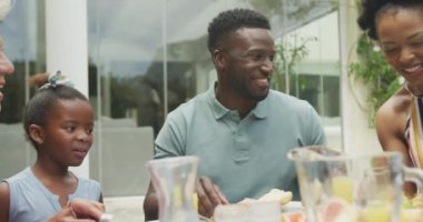 Mutlu Afro-Amerikan ailesi konuşuyor ve bahçede kahvaltı yapıyor. Aile birlikte dışarıda vakit geçiriyor..