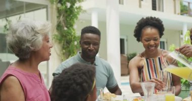 Mutlu Afro-Amerikan ailesi meyve suyu içip bahçede kahvaltı yapıyor. Aile birlikte dışarıda vakit geçiriyor..