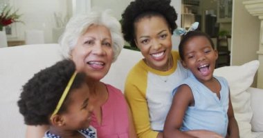 Yetişkin kızları ve torunları oturma odasında olan mutlu Afrikalı Amerikalı büyükannenin portresi. Aile evde birlikte vakit geçiriyor..