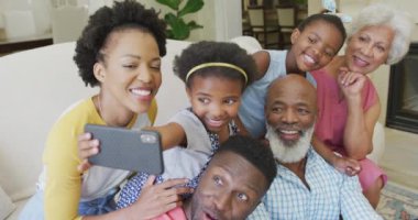 Mutlu Afro-Amerikan ailesi oturma odasında oturup akıllı telefon kullanıyor. Aile evde birlikte vakit geçiriyor..