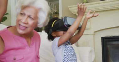 Torunları olan mutlu Afro-Amerikan büyükanne oturma odasında VR kulaklık kullanıyor. Aile evde birlikte vakit geçiriyor..
