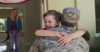 Caucasian male soldier embracing his smiling son over wife and american flag. soldier returning home to family.