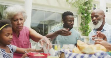 Mutlu Afro-Amerikan ailesi meyve suyu doldurup bahçede kahvaltı yapıyor. Aile birlikte dışarıda vakit geçiriyor..