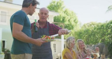 Kafkasyalı mutlu bir aile bahçede barbekü yapıp yemek yiyor. Aile evde birlikte vakit geçiriyor..