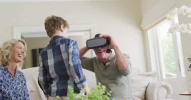 Happy senior caucasian couple with grandson using vr headset in living room. family spending time together at home.