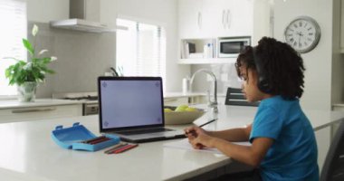Masada oturan mutlu melez çocuk fotokopi alanı olan dizüstü bilgisayar kullanıyor ve online dersler alıyor. ev hayatı, evde zaman geçirmek..