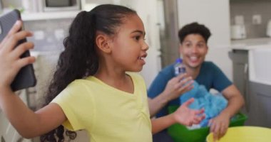 Mutlu çift ırklı baba-kız video görüşmeleri akıllı telefon kullanarak, birlikte atık ayıklayarak. ev hayatı, evde boş zaman geçirmek..