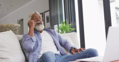 Akıllı telefon ve dizüstü bilgisayar kullanan Afro-Amerikan bir adamın videosu. Emeklilik yaşam tarzı, ev konseptinde dijital olarak oluşturulmuş video ile zaman geçirme.