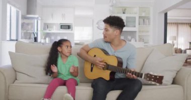 Mutlu çift ırklı baba ve kız kanepede oturup gitar çalıyor. ev hayatı, evde boş zaman geçirmek..