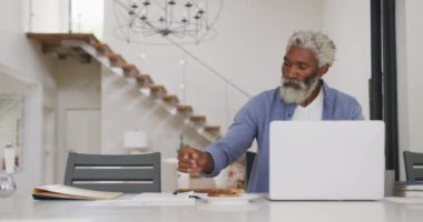 Dizüstü bilgisayar kullanan Afro-Amerikan kıdemli bir adamın videosu. Emeklilik yaşam tarzı, ev konseptinde dijital olarak oluşturulmuş video ile zaman geçirme.